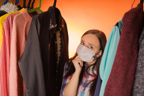 Nahaufnahme einer jungen, traurigen Frau, die zwischen Kleidern steht, die sich nicht für die Wahl der Kleidung im Kleiderschrank entscheiden können. — Stockfoto