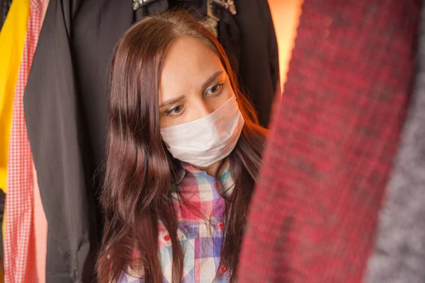 Nahaufnahme einer jungen Frau in medizinischer Maske, die sich umschaut und überlegt, was sie im Kleiderschrank anziehen soll. — Stockfoto