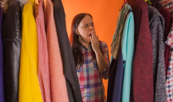 Close-up van jonge vrouw staan tussen kleren en gapen van nadenken wat te kiezen kleding in garderobe. — Stockfoto