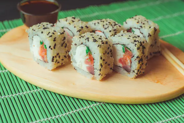 Primo piano di gustosi involtini di sushi su tavola di legno con salsa di soia e bacchette su tovagliolo di bambù decorativo . — Foto Stock