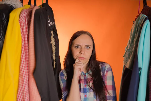 年轻的女人站在衣柜里的衣服中间鬼鬼祟祟的.成年女性选择商店里的东西. — 图库照片