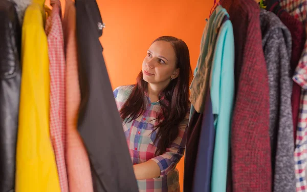 Jonge vrouw grimmig staande tussen kleren in de kast. Volwassen vrouw die dingen in petto heeft. — Stockfoto