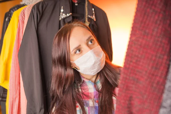 Крупный план молодой женщины в медицинской маске оглядываясь вокруг, размышляя, что выбрать одежду в гардеробе . — стоковое фото