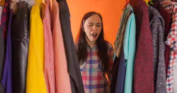 Close-up van jonge vrouw staan tussen kleren en gapen van nadenken wat te kiezen kleding in garderobe. — Stockfoto