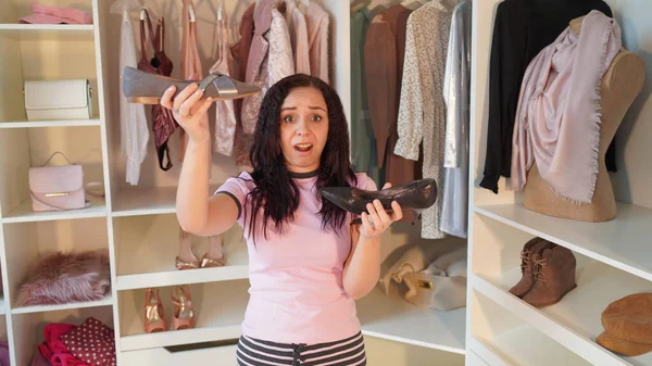 Portret van een geschokte jonge vrouw, met schoenen in haar handen in de kleedkamer. Charmante vrouw nadenken over wat te kiezen slipper in de kast. — Stockfoto