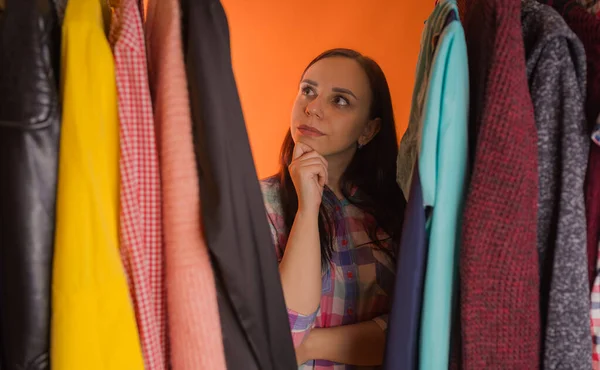 Jonge vrouw grimmig staande tussen kleren in de kast. Volwassen vrouw die dingen in petto heeft. — Stockfoto