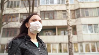 Sokakta duran tıbbi maske takmış genç bir kadının portresi. Yetişkin kadın kendini hastalıklardan korumak için yüzünü maskeyle örttü..