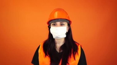 Turuncu arka planda yüzünde tıbbi maske takan genç bir kadının portresi. Yetişkin bir kadın kendini hastalıklardan korumak için yüzünü maskeyle örttü. Koronavirüs salgını veya hastalıklar kavramı.