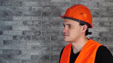 Tulumlu erkek inşaat işçisi, gri tuğla duvarın arka planına tıbbi maske takıyor.