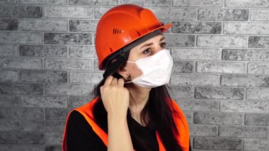 Tulumlu kadın inşaat işçisi gri tuğla duvarın arka planındaki tıbbi maskeyi çıkarıyor.