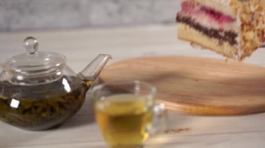 Tahtadaki kekin bir parçasını çaydanlıkta yeşil çay ve beyaz ahşap masada fincan ile kapat..