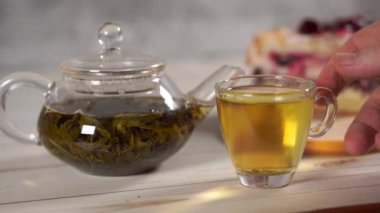 Çaydanlıktaki yeşil çayı ve beyaz tahta masadaki fincanı kapat..