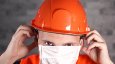 Tulumlu erkek inşaat işçisi, gri tuğla duvarın arka planına tıbbi maske takıyor.