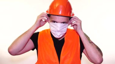 Tulumlu erkek inşaat işçisi beyaz arka plana tıbbi maske takıyor..