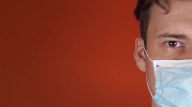 Turuncu bir arka planda yüzünde tıbbi maske olan bir adam. Coronavirüs Salgını.