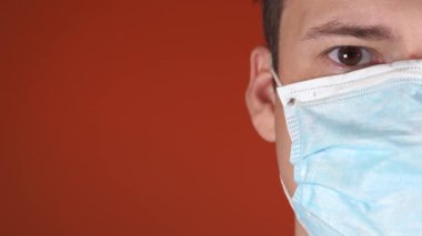 Turuncu bir arka planda yüzünde tıbbi maske olan bir adam. Coronavirüs Salgını.