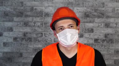 Gri tuğla duvarın arka planında tıbbi maskeli genç bir adamın portresi. Yetişkin erkek, kendini hastalıklardan korumak için maske takıyor. Koronavirüs salgını veya hastalıklar kavramı.