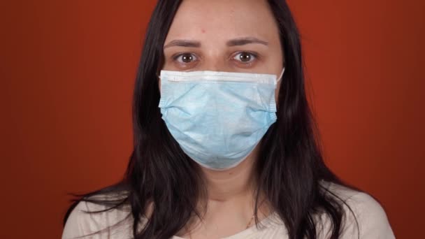 En kvinna med en medicinsk mask på ansiktet på en orange bakgrund. Coronavirusets epidemi. — Stockvideo