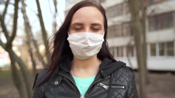 Portrait of young woman in medical mask on her face standing on street. Adult female covered her face with mask to protect yourself from diseases. — Stock Video