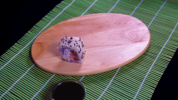 Primer plano de sabrosos rollos de sushi sobre tabla de madera con salsa de soja y palillos en servilleta de bambú decorativa . — Vídeos de Stock