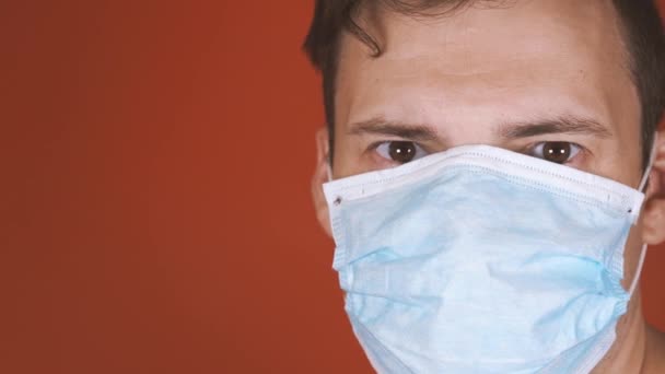 En man med en medicinsk mask på ansiktet på en orange bakgrund. Coronavirusets epidemi. — Stockvideo