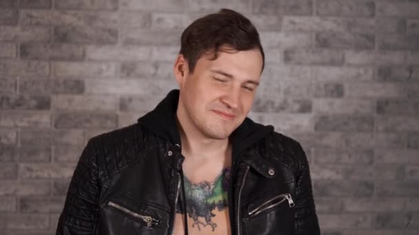 A man in a fancy jacket with a tattoo on his chest. Portrait of a young man in a leather jacket, smiling at the camera on a white background — Stock Video
