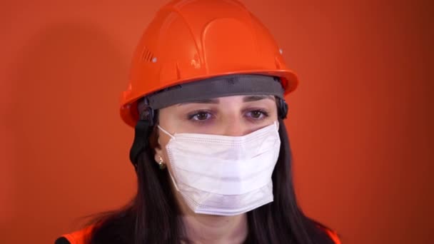 Trabalhadora da construção feminina em macacão e máscara médica tosse em fundo laranja. Conceito de ameaça de infecção . — Vídeo de Stock