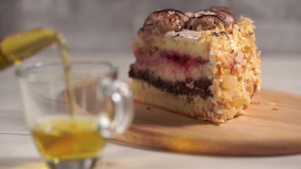 Gros plan du morceau de gâteau sur une planche en bois avec du thé vert dans une théière et une tasse sur une table en bois blanc . — Video