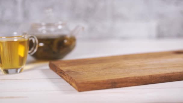 Primer plano del pedazo de pastel sobre tabla de madera con té verde en tetera y taza sobre mesa de madera blanca . — Vídeos de Stock