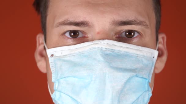 Egy férfi orvosi maszkkal az arcán, narancssárga háttérrel. A koronavírus járványa. — Stock videók