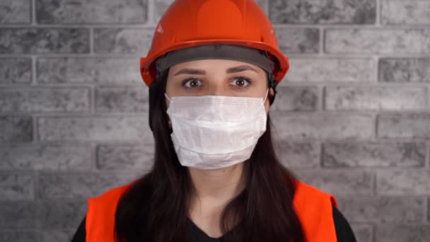 Портрет молодой женщины в медицинской маске на ее лице на фоне серой кирпичной стены. Взрослая женщина закрыла лицо маской, чтобы защитить себя от болезней. Понятие эпидемии коронавируса или — стоковое видео