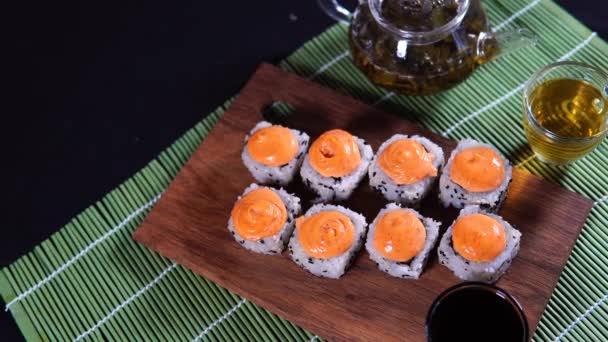 Primer plano de sabrosos rollos de sushi sobre tabla de madera con salsa de soja en servilleta de bambú decorativa. Mujeres mano poniendo rollos de sushi con palillos en la tabla de cortar . — Vídeo de stock