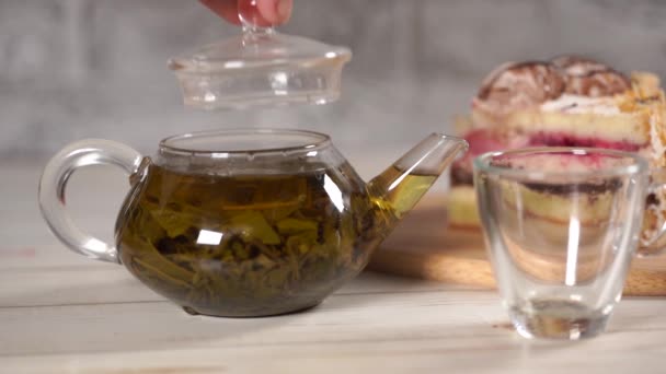 Närbild av grönt te i tekanna och kopp på vitt träbord. — Stockvideo