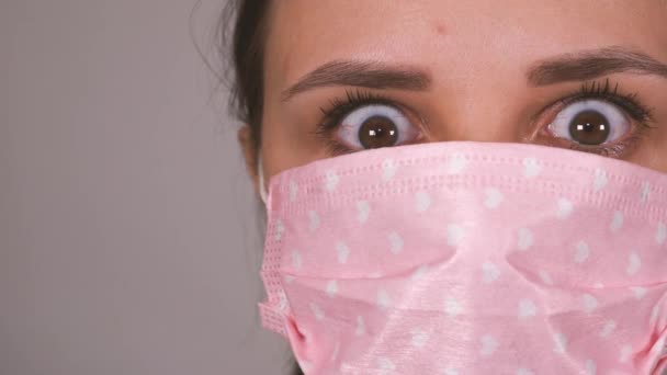 En kvinna med en medicinsk mask på ansiktet på en grå bakgrund. Coronavirusets epidemi. — Stockvideo