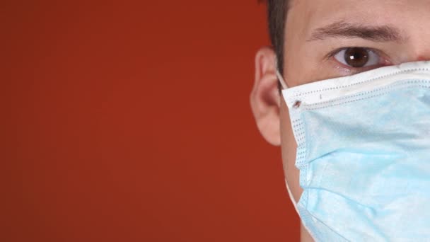 Een man met een medisch masker op zijn gezicht op een oranje achtergrond. De Epidemie van het Coronavirus. — Stockvideo