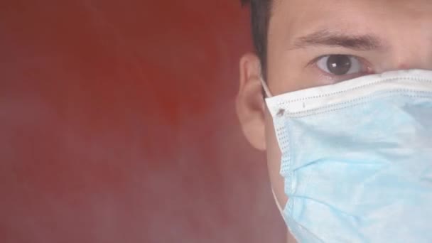 Man met een medisch masker op zijn gezicht. Close-up van het mannelijke deel van het gezicht dat in de camera kijkt. Een volwassene bedekte zijn gezicht met een masker van rook. Begrip rookverbod. — Stockvideo