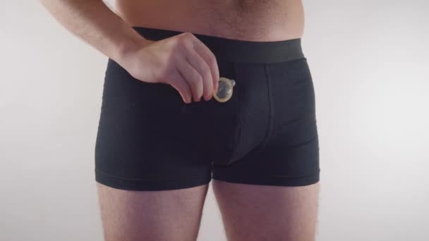 Närbild av en man i underkläder håller en kondom på en vit bakgrund. Man i underkläder med kondom och preventivmedel. Preventivmedel - man i underkläder — Stockvideo