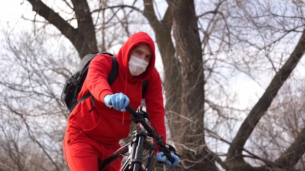 Молодой человек в медицинской маске и перчатках сидит на велосипеде в сельской местности. Мужчина защищает себя от болезней во время ходьбы. Концепция угрозы коронавирусной эпидемии . — стоковое фото