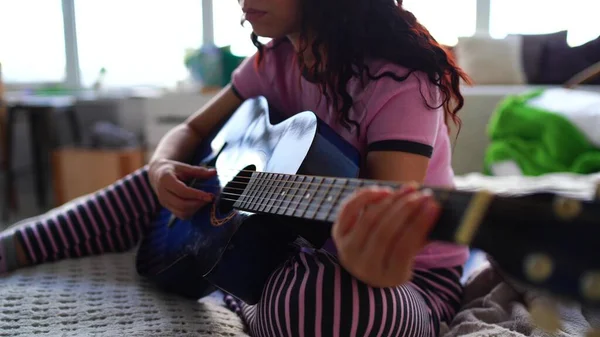 Молода жінка грає на гітарі в спальні. Молода жінка грає на гітарі у ліжку. Вона насолоджується вільним часом. Красива дівчина грає на гітарі в затишній спальні — стокове фото
