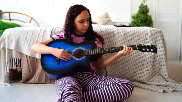 Młoda kobieta grająca na gitarze w sypialni. Młoda kobieta grająca na gitarze w łóżku. Lubi swój wolny czas. Piękna dziewczyna grać na gitarze w przytulnej sypialni — Zdjęcie stockowe