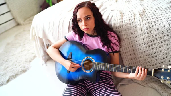 Młoda kobieta grająca na gitarze w sypialni. Młoda kobieta grająca na gitarze w łóżku. Lubi swój wolny czas. Piękna dziewczyna grać na gitarze w przytulnej sypialni — Zdjęcie stockowe