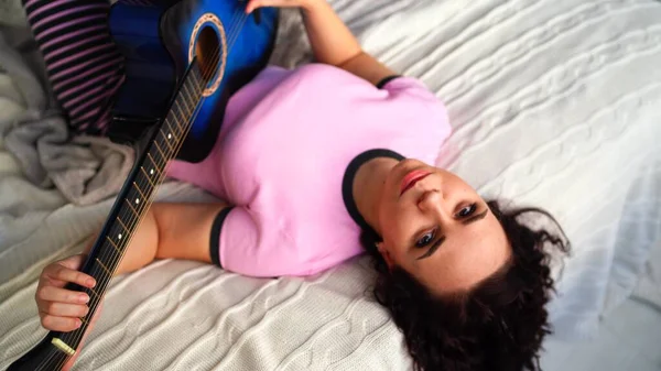 Jeune femme jouant de la guitare dans la chambre. Jeune femme jouant de la guitare dans son lit. Elle aime son temps libre. Belle fille jouer de la guitare dans une chambre confortable — Photo