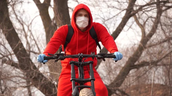 Ung man i medicinsk mask och handskar hosta på landsbygden. Vuxen man i röd kostym skyddar dig från sjukdomar på promenad. Begreppet hot om infektion med coronavirus. — Stockfoto