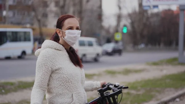 Молодая женщина в медицинской маске стоит с велосипедом на городской улице. Взрослая женщина покрывает лицо маской, чтобы защитить себя от болезней во время ходьбы. Концепция угрозы коронавирусной эпидемии . — стоковое фото