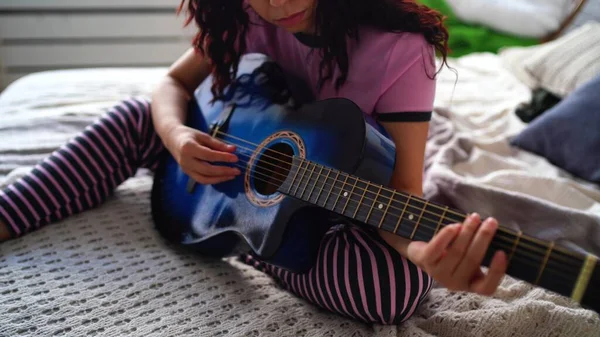 Giovane donna che suona la chitarra in camera da letto. Primo piano mano femminile suonare una corda di chitarra. — Foto Stock