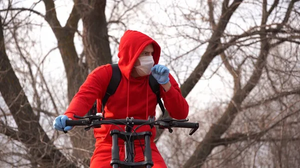 Молодий чоловік в медичній масці і кашляє рукавички, сидячи на велосипеді в сільській місцевості. Дорослий чоловік у червоному костюмі захищає себе від хвороб на прогулянці. Концепція загрози коронавірусної інфекції . — стокове фото