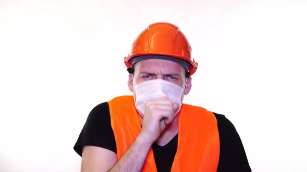 Мужчина строитель в комбинезоне и медицинская маска, кашляющая на белом фоне. Концепция угрозы заражения . — стоковое фото