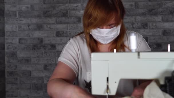 Close-up van volwassen vrouw naaien gordijn, met behulp van naaimachine. Jonge naaister in medisch masker werkt aan naaimachine thuis. — Stockvideo