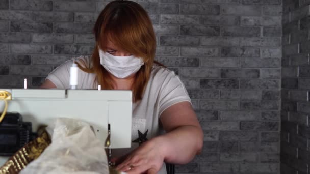 Primer plano de la mujer adulta costura cortina, utilizando la máquina de coser. Joven costurera en máscara médica trabajando en la máquina de coser en casa . — Vídeo de stock