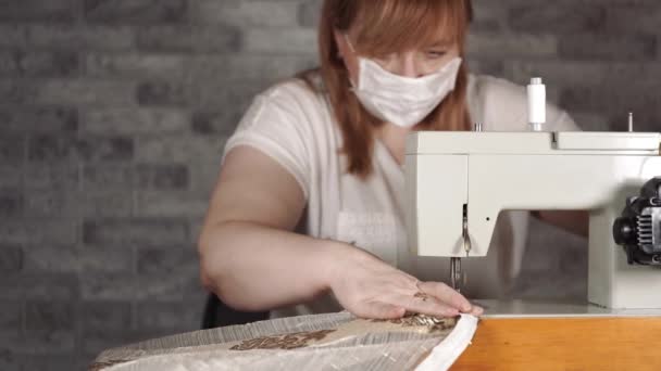 Close-up van volwassen vrouw naaien gordijn, met behulp van naaimachine. Jonge naaister in medisch masker werkt aan naaimachine thuis. — Stockvideo